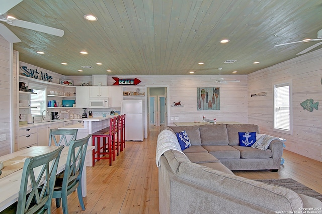 living room featuring plenty of natural light, wood walls, ceiling fan, and light hardwood / wood-style floors