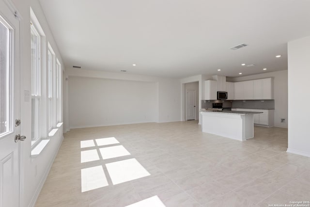 kitchen with range, a kitchen island with sink, tasteful backsplash, light stone countertops, and white cabinets