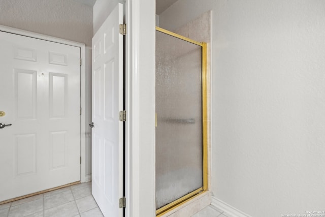 bathroom with a textured ceiling, a shower with door, and tile patterned floors