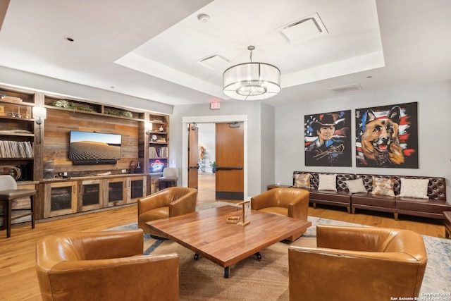 living room with a notable chandelier, a tray ceiling, built in features, and hardwood / wood-style floors