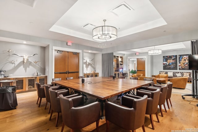 dining space featuring an inviting chandelier, a tray ceiling, and light wood-type flooring