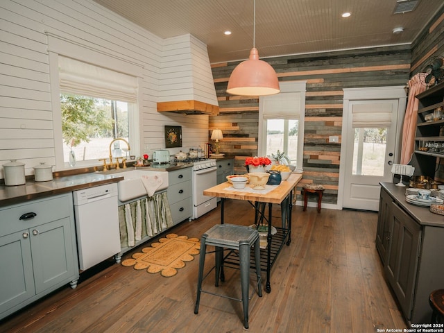 kitchen with white appliances, sink, dark hardwood / wood-style floors, wood walls, and custom range hood