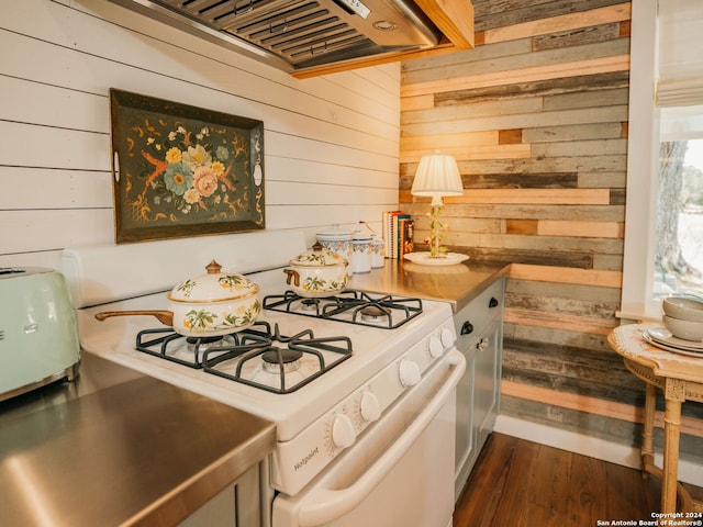 kitchen with dark hardwood / wood-style floors, white range with gas stovetop, custom exhaust hood, and wooden walls