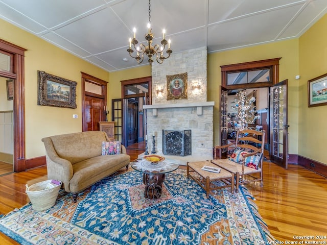 living room with a stone fireplace, a chandelier, and wood-type flooring