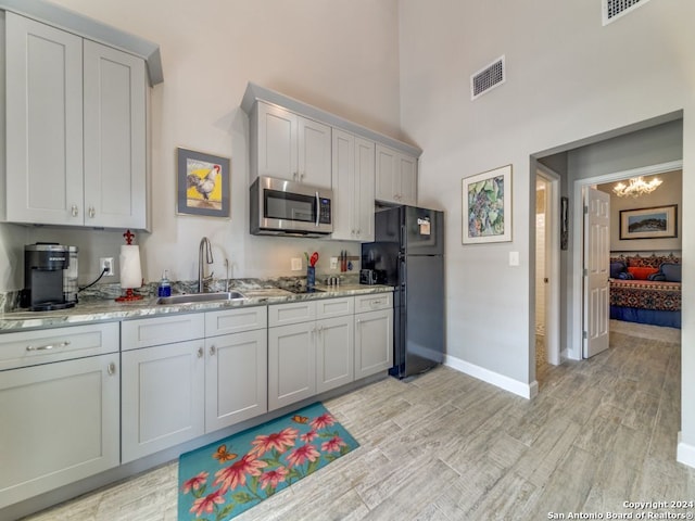 kitchen featuring light stone counters, black fridge, a towering ceiling, an inviting chandelier, and sink