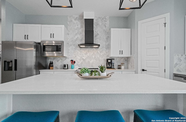 kitchen featuring appliances with stainless steel finishes, a breakfast bar area, wall chimney exhaust hood, white cabinets, and decorative backsplash