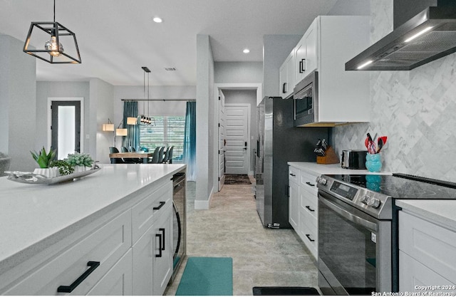 kitchen featuring hanging light fixtures, wall chimney exhaust hood, stainless steel appliances, decorative backsplash, and white cabinetry