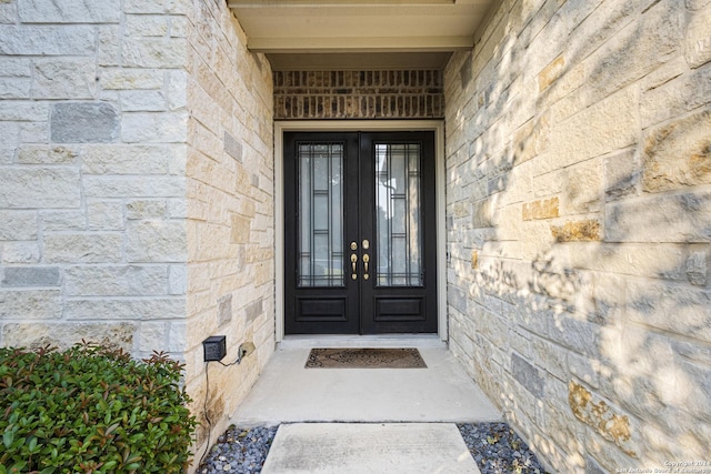 view of exterior entry with stone siding, french doors, and brick siding