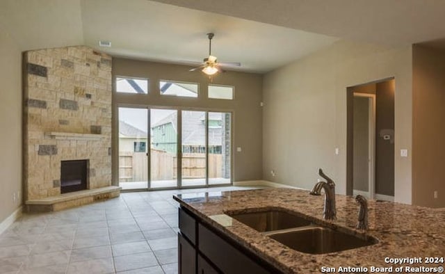 kitchen with sink, ceiling fan, light tile patterned floors, a fireplace, and stone countertops