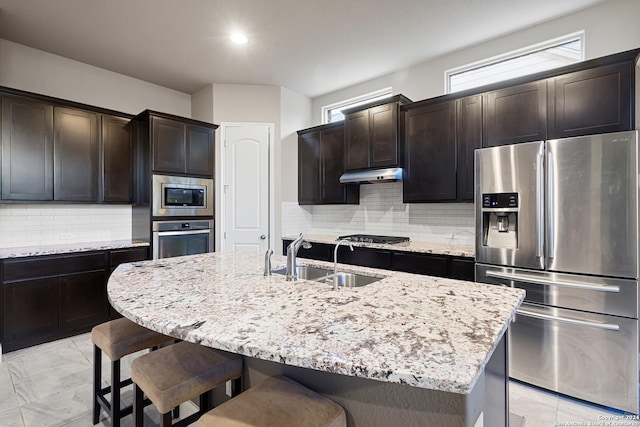 kitchen featuring dark brown cabinetry, sink, tasteful backsplash, an island with sink, and appliances with stainless steel finishes