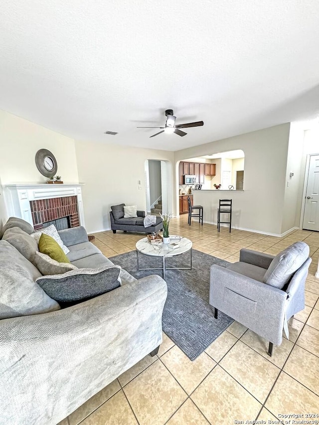 living room with a brick fireplace, ceiling fan, and light tile patterned flooring