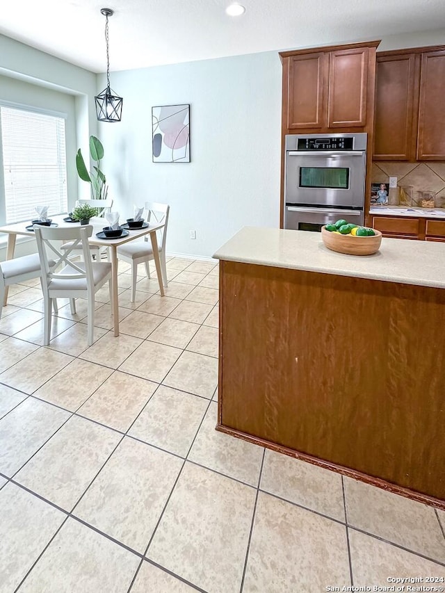 kitchen featuring pendant lighting, stainless steel double oven, tasteful backsplash, and light tile patterned floors