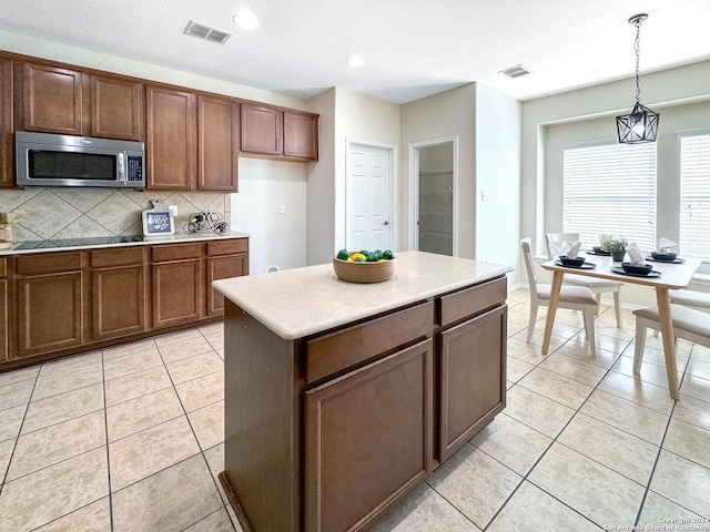 kitchen featuring pendant lighting, a center island, backsplash, light tile patterned floors, and black electric cooktop