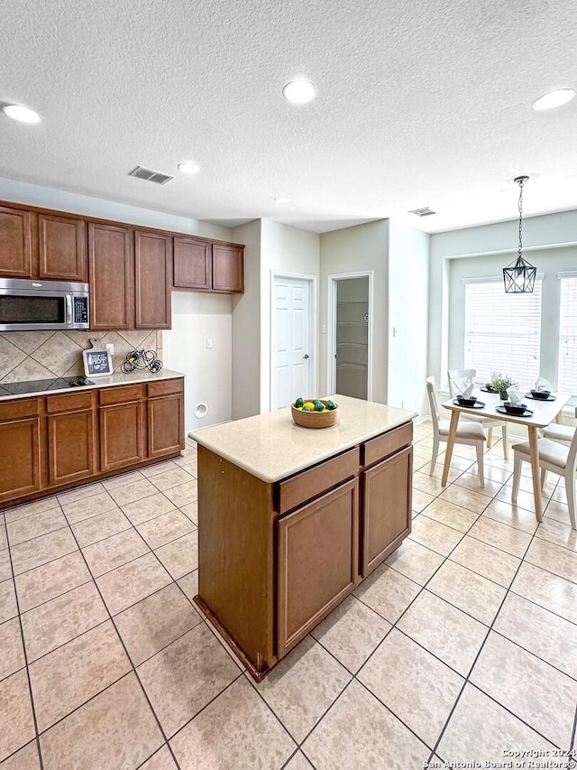 kitchen featuring light tile patterned floors, tasteful backsplash, pendant lighting, a textured ceiling, and a kitchen island