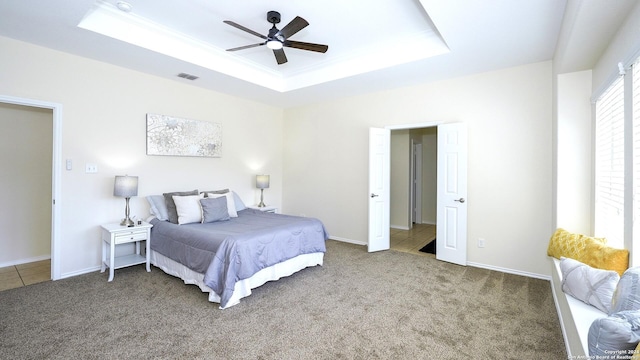 carpeted bedroom featuring a tray ceiling and ceiling fan