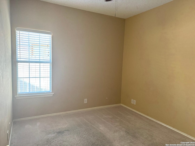 empty room with a textured ceiling, plenty of natural light, and carpet flooring