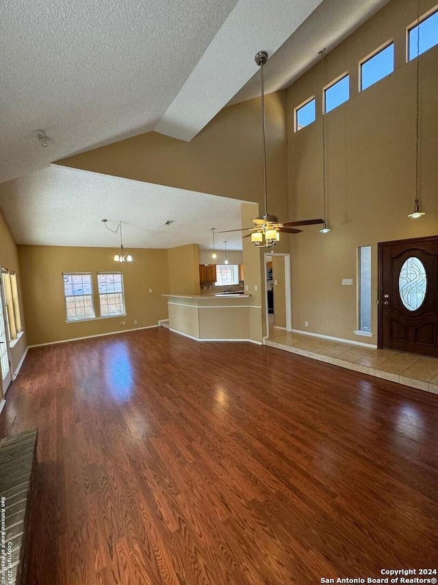 unfurnished living room featuring lofted ceiling, hardwood / wood-style floors, ceiling fan with notable chandelier, and a textured ceiling