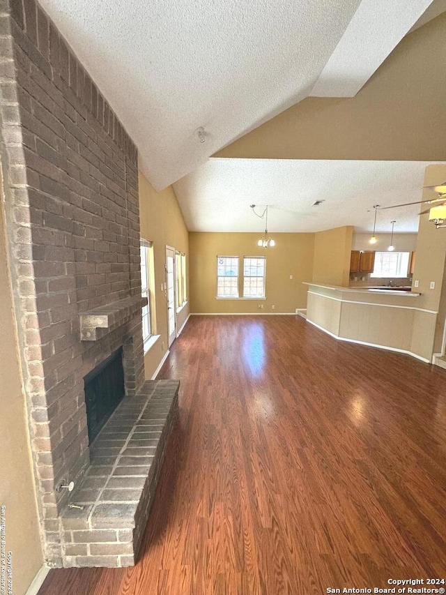 unfurnished living room featuring vaulted ceiling, a brick fireplace, dark wood-type flooring, and a textured ceiling