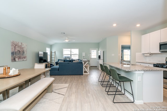 kitchen featuring white cabinets, backsplash, light stone counters, stainless steel appliances, and light hardwood / wood-style floors