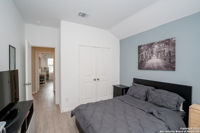 bedroom with lofted ceiling, visible vents, baseboards, light wood-style floors, and a closet