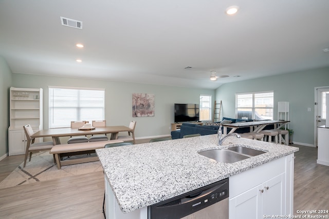 kitchen with a center island with sink, light hardwood / wood-style floors, light stone counters, and sink