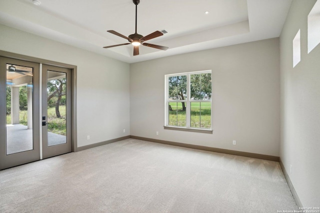 unfurnished room featuring light carpet, a tray ceiling, french doors, and ceiling fan