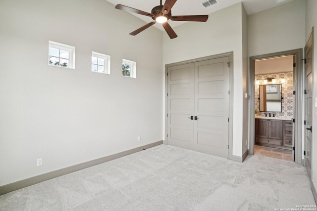 unfurnished bedroom featuring light carpet, ensuite bathroom, a closet, and a high ceiling