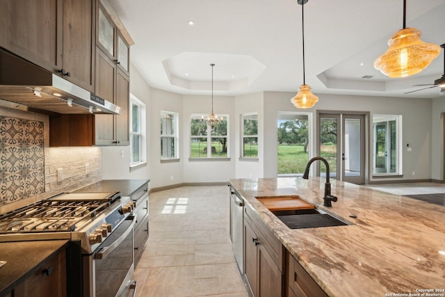 kitchen featuring sink, light stone counters, appliances with stainless steel finishes, a tray ceiling, and pendant lighting