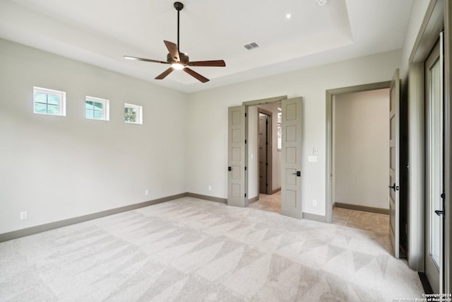 unfurnished bedroom featuring ceiling fan, light colored carpet, and a tray ceiling