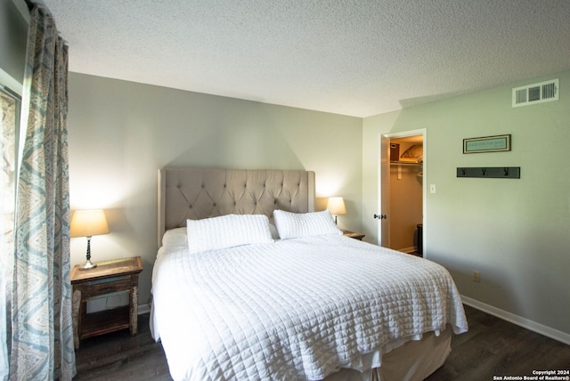 bedroom featuring dark wood-type flooring, a textured ceiling, a closet, and a walk in closet