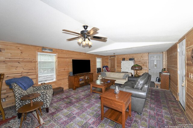 living room with ceiling fan, wood walls, and lofted ceiling