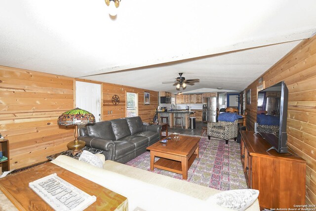 living room featuring vaulted ceiling, ceiling fan, and wooden walls