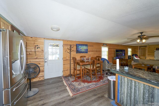 dining room with vaulted ceiling, wood walls, dark hardwood / wood-style flooring, and a healthy amount of sunlight