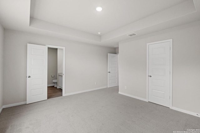 unfurnished bedroom featuring a raised ceiling, ensuite bath, and carpet floors