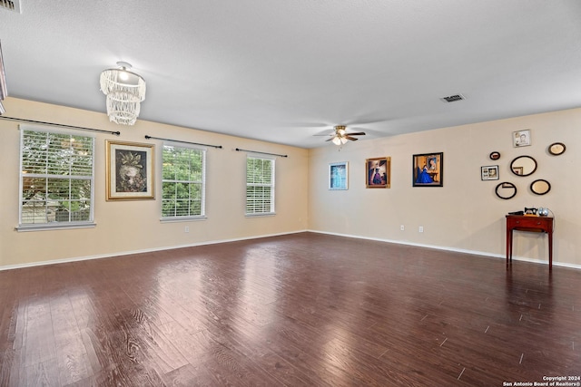 empty room featuring dark hardwood / wood-style floors, ceiling fan with notable chandelier, and plenty of natural light