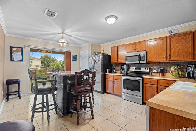 kitchen with a textured ceiling, appliances with stainless steel finishes, backsplash, light tile patterned flooring, and a breakfast bar area