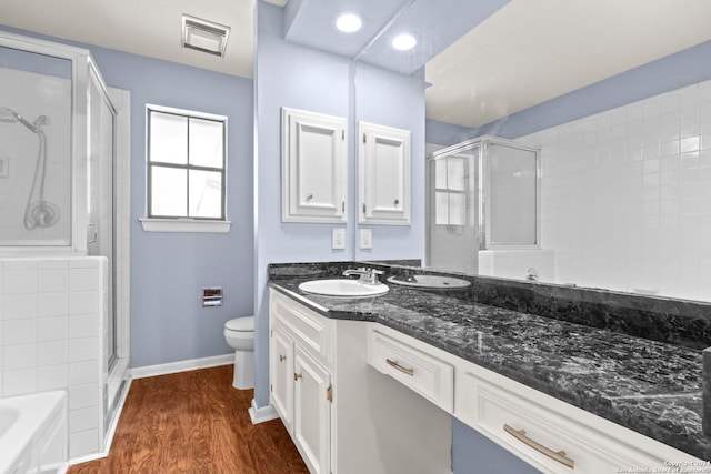 bathroom with hardwood / wood-style floors, vanity, a shower with shower door, and toilet