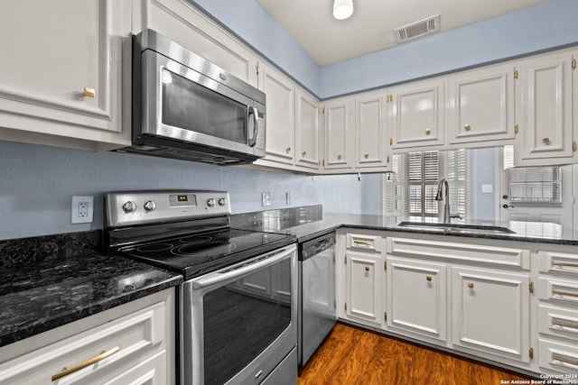 kitchen featuring dark wood-type flooring, dark stone counters, white cabinets, sink, and stainless steel appliances