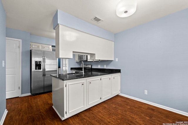 kitchen with white cabinets, appliances with stainless steel finishes, kitchen peninsula, and dark stone countertops