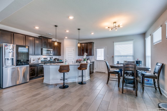 kitchen with stainless steel appliances, hanging light fixtures, a center island, light stone counters, and dark brown cabinetry