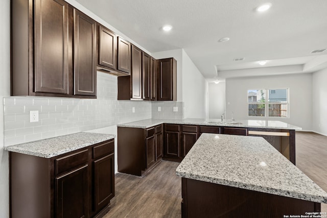 kitchen with dark brown cabinetry, backsplash, dark wood-type flooring, and kitchen peninsula