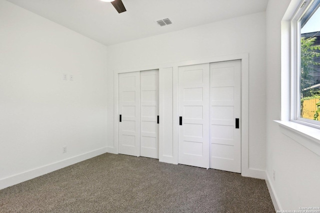 unfurnished bedroom featuring dark colored carpet, ceiling fan, and multiple closets