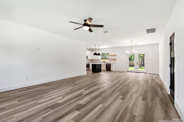 unfurnished living room featuring hardwood / wood-style flooring, ceiling fan with notable chandelier, and french doors