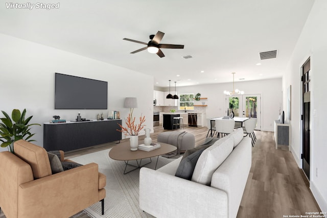 living room featuring french doors, ceiling fan with notable chandelier, and light hardwood / wood-style flooring