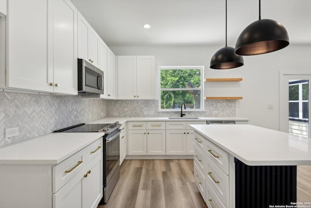 kitchen with white cabinets, sink, light hardwood / wood-style flooring, decorative light fixtures, and stainless steel appliances