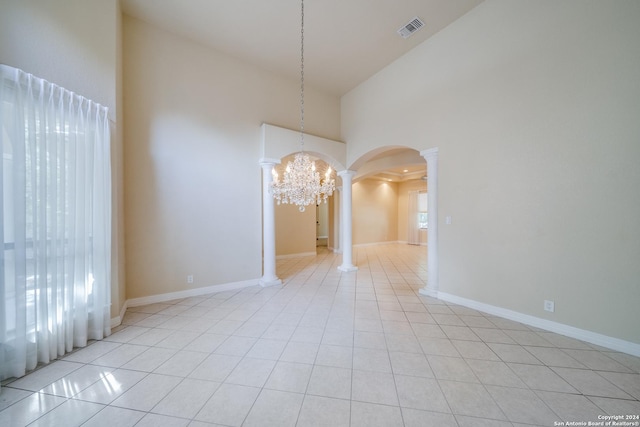 spare room with decorative columns, light tile patterned flooring, a high ceiling, and a notable chandelier