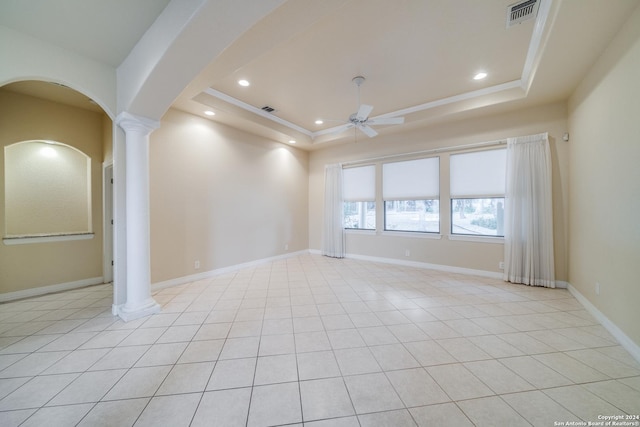 empty room with a tray ceiling, ornate columns, ceiling fan, and light tile patterned flooring