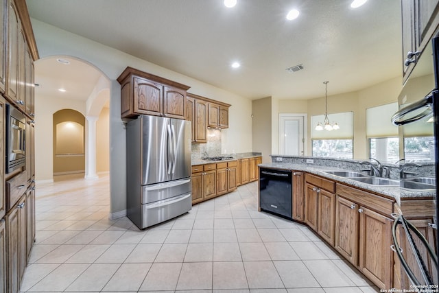 kitchen featuring appliances with stainless steel finishes, tasteful backsplash, light stone counters, pendant lighting, and an inviting chandelier