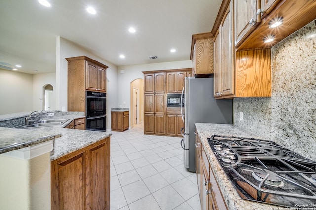 kitchen with light stone countertops, sink, backsplash, light tile patterned floors, and black appliances