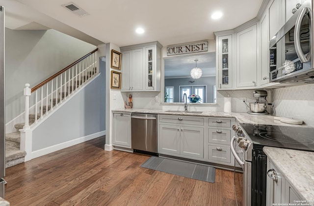 kitchen featuring dark wood-type flooring, stainless steel appliances, sink, hanging light fixtures, and light stone counters